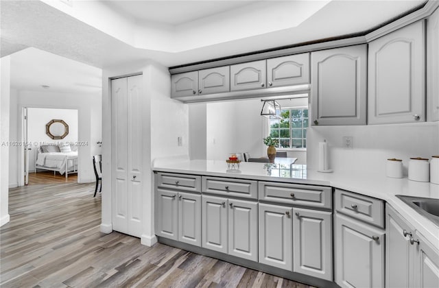 kitchen with gray cabinets, a raised ceiling, and light hardwood / wood-style flooring