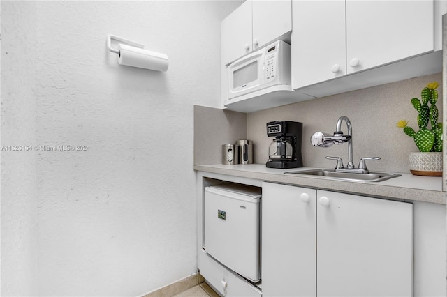 kitchen featuring fridge, sink, white microwave, and white cabinets