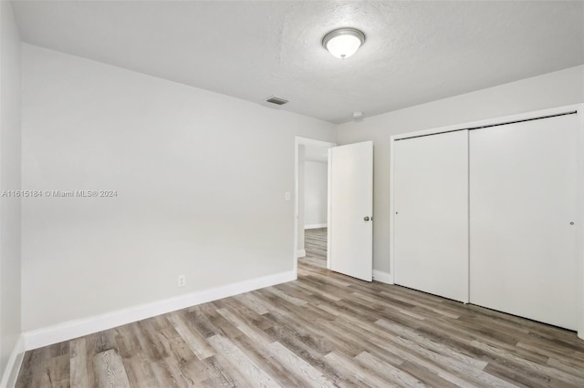 unfurnished bedroom featuring a closet, a textured ceiling, and light wood-type flooring