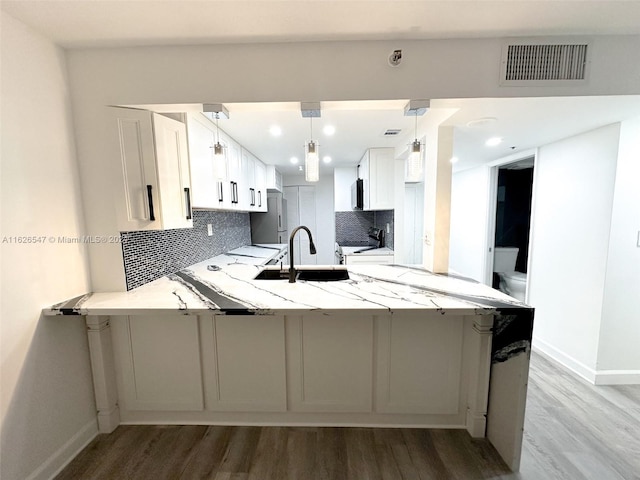 kitchen featuring pendant lighting, kitchen peninsula, light stone counters, decorative backsplash, and wood-type flooring