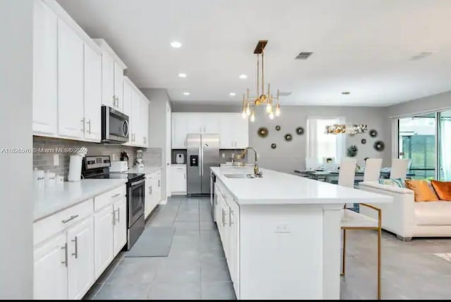 kitchen with white cabinets, an island with sink, sink, appliances with stainless steel finishes, and light tile patterned floors