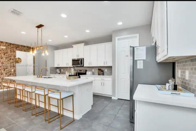 kitchen with light tile patterned flooring, white cabinets, a kitchen island with sink, stainless steel appliances, and sink