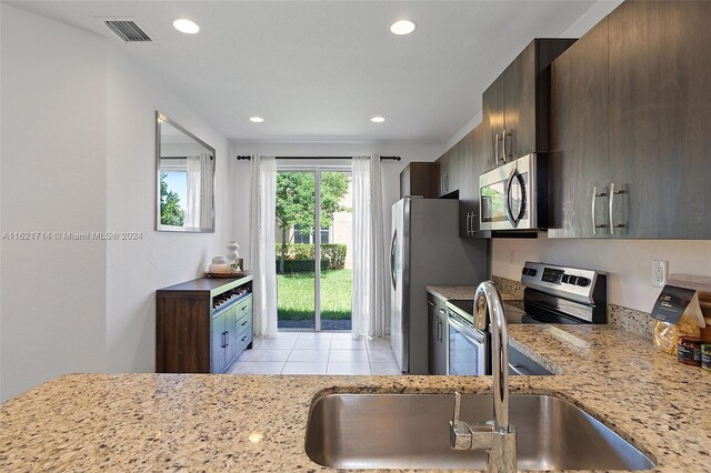 kitchen featuring dark brown cabinets, light tile patterned floors, light stone counters, and sink