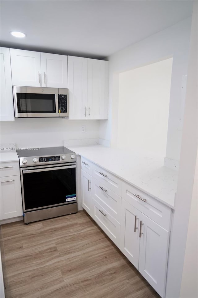 kitchen featuring light hardwood / wood-style flooring, white cabinetry, light stone counters, and stainless steel appliances