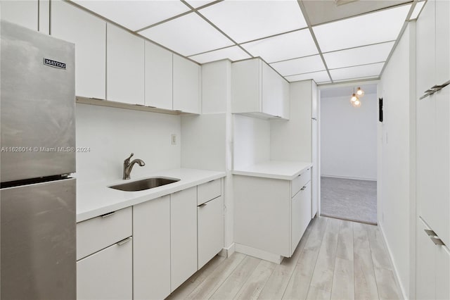 kitchen with white cabinetry, a drop ceiling, stainless steel refrigerator, light colored carpet, and sink