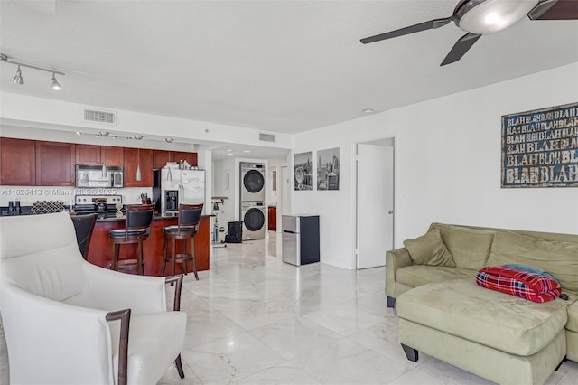 living room featuring ceiling fan, stacked washer and clothes dryer, and a textured ceiling