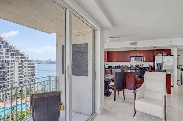 kitchen with a water view, stainless steel appliances, rail lighting, and a textured ceiling