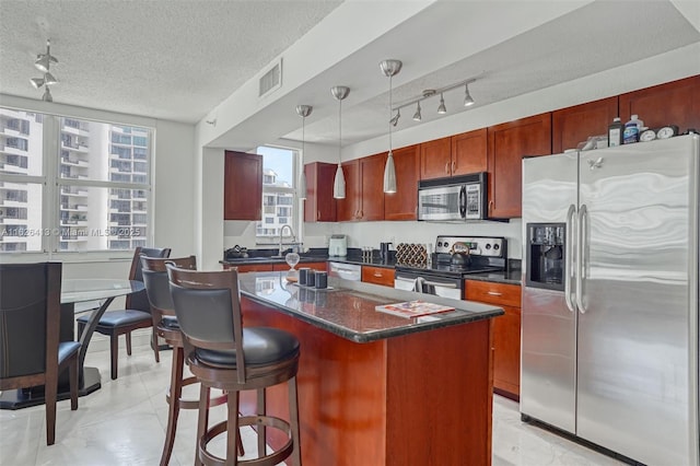 kitchen featuring appliances with stainless steel finishes, a textured ceiling, pendant lighting, a kitchen island, and sink