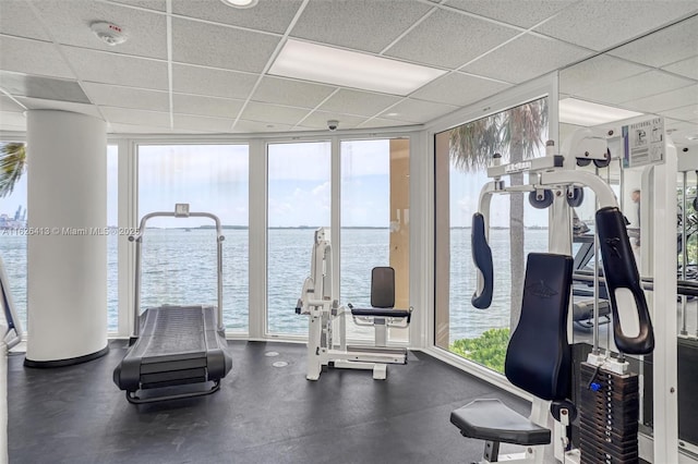 workout area with a paneled ceiling, a wall of windows, and a water view