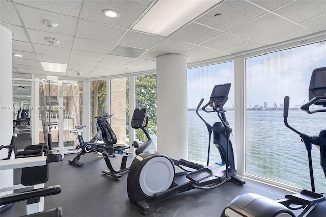 exercise room with a paneled ceiling, a water view, and expansive windows