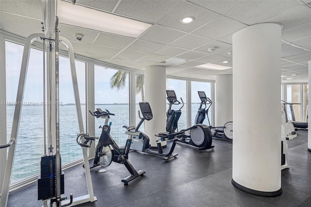 exercise room featuring a wall of windows, a water view, a wealth of natural light, and a paneled ceiling