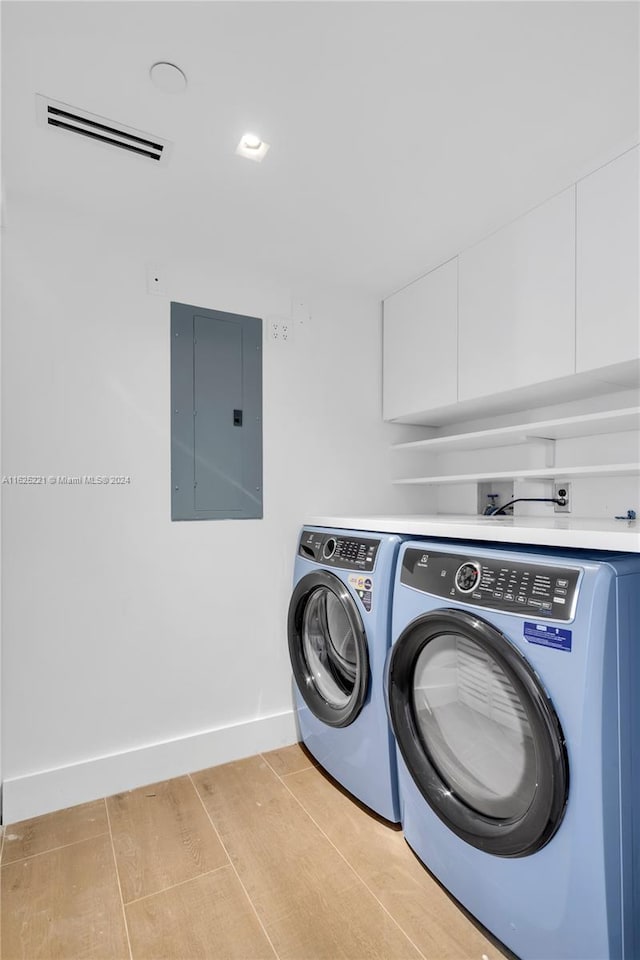 clothes washing area with independent washer and dryer, electric panel, and light wood-type flooring