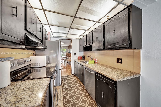 kitchen featuring sink, tasteful backsplash, light stone countertops, and appliances with stainless steel finishes