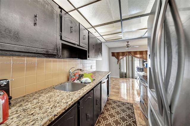 kitchen featuring light stone countertops, appliances with stainless steel finishes, decorative backsplash, sink, and ceiling fan