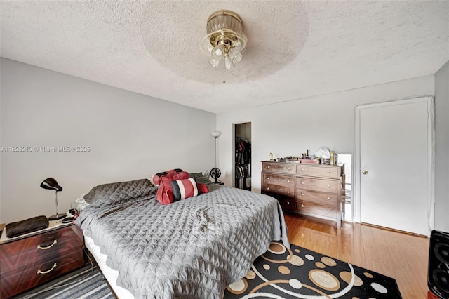 bedroom featuring a textured ceiling, a walk in closet, hardwood / wood-style flooring, a closet, and ceiling fan