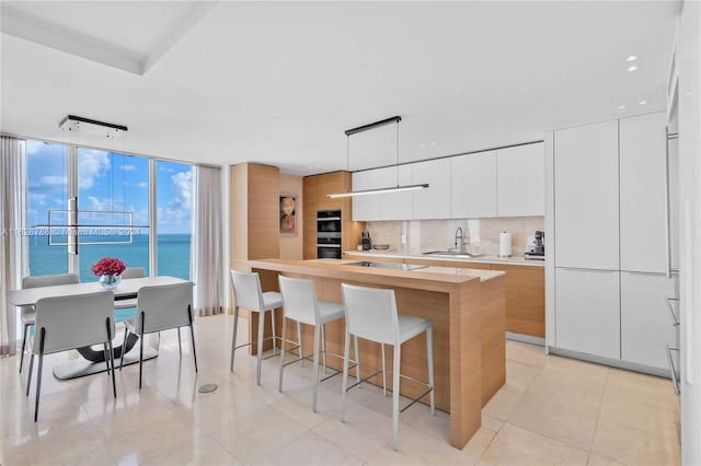 kitchen with sink, a water view, hanging light fixtures, a kitchen island with sink, and white cabinets