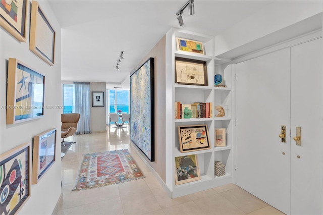 hall featuring light tile patterned flooring, track lighting, and built in shelves