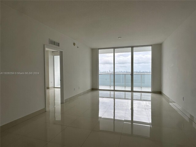 tiled spare room with a water view and floor to ceiling windows