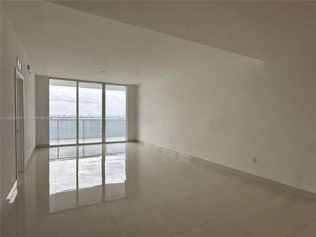 empty room featuring a water view, light tile patterned floors, and floor to ceiling windows