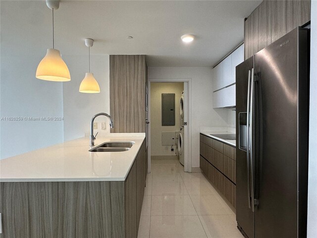 kitchen with light tile patterned floors, stainless steel refrigerator with ice dispenser, sink, stacked washer / drying machine, and pendant lighting