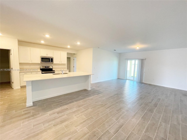 kitchen featuring light wood finished floors, light countertops, appliances with stainless steel finishes, open floor plan, and a sink