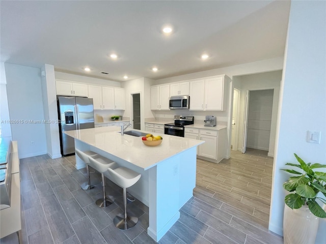 kitchen with white cabinets, appliances with stainless steel finishes, a breakfast bar, wood tiled floor, and a sink