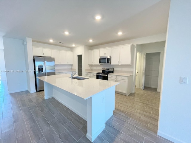 kitchen featuring a kitchen island with sink, wood finish floors, a sink, white cabinets, and appliances with stainless steel finishes