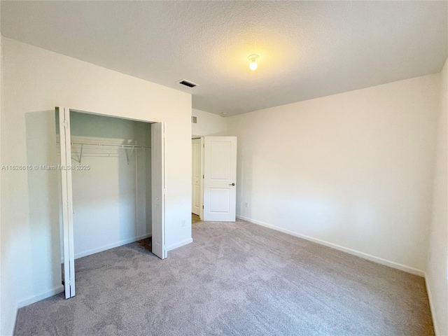 unfurnished bedroom with a textured ceiling, carpet floors, visible vents, baseboards, and a closet