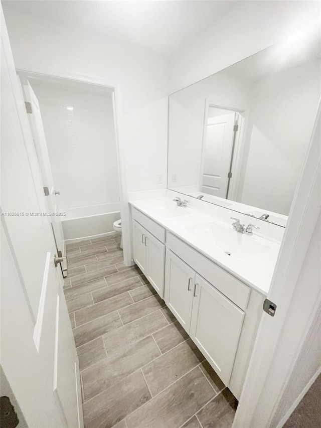 full bathroom featuring toilet, double vanity, a sink, and wood finish floors