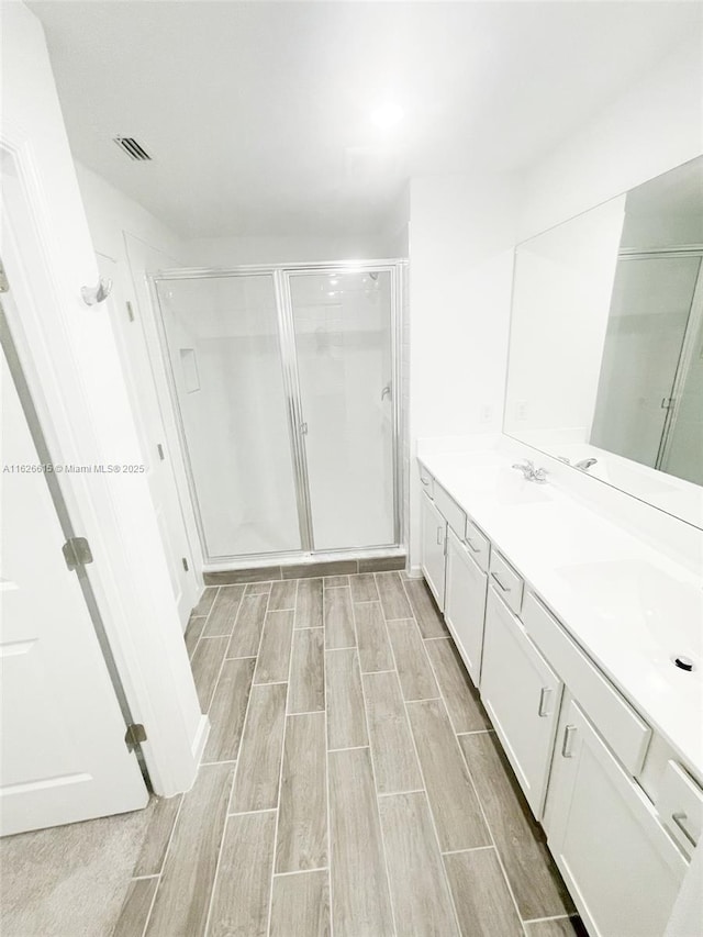 full bathroom featuring wood finish floors, a sink, a shower stall, and double vanity