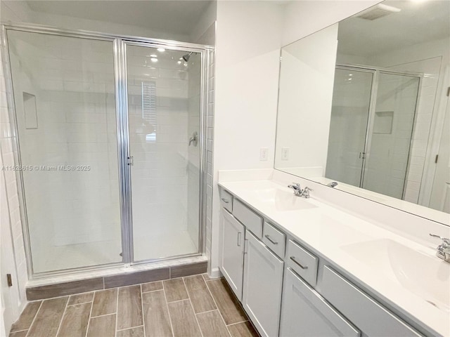 full bath featuring wood finish floors, a sink, a shower stall, and double vanity