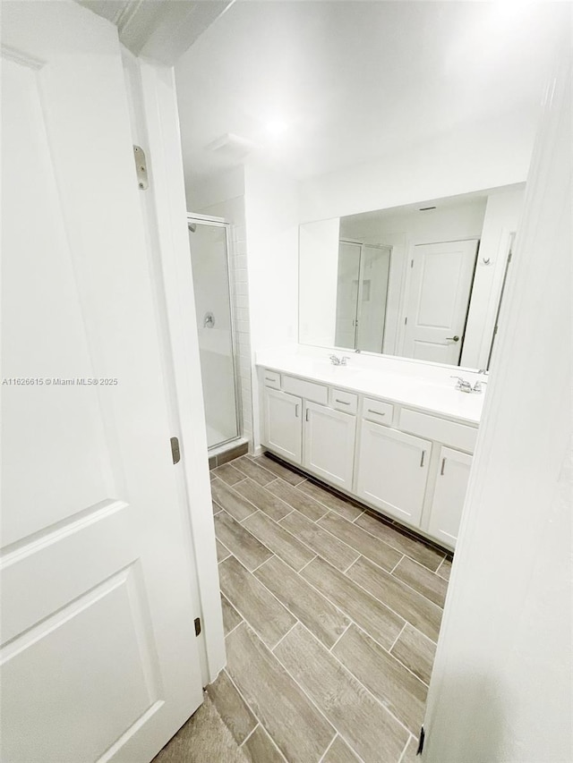 bathroom featuring a sink, double vanity, wood finish floors, and a shower stall