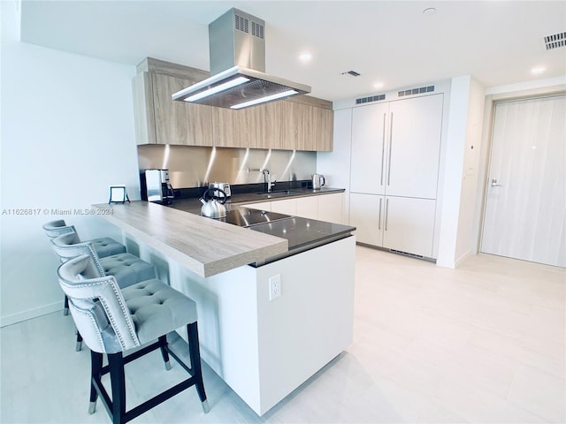 kitchen with island range hood, sink, a kitchen breakfast bar, black electric stovetop, and kitchen peninsula