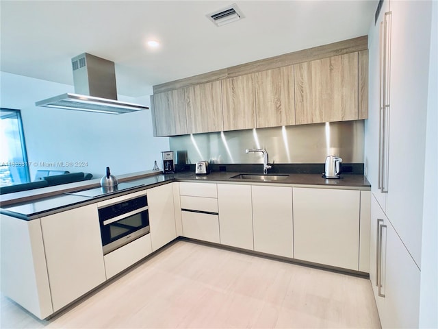 kitchen featuring cooktop, sink, light brown cabinets, oven, and range hood