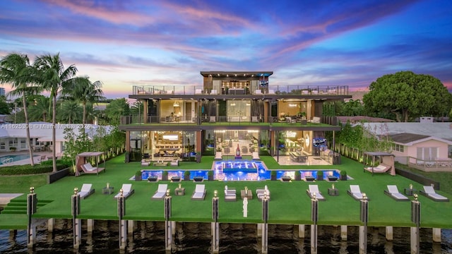 back house at dusk with a balcony, a water view, and a patio area