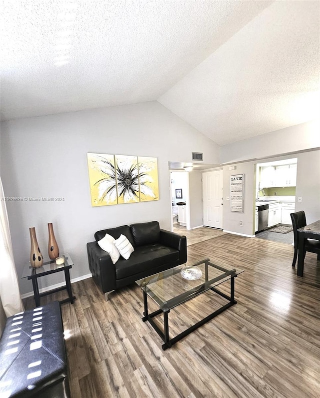 living room with lofted ceiling, hardwood / wood-style floors, sink, and a textured ceiling