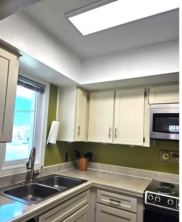 kitchen with electric range, sink, stainless steel counters, and white cabinets