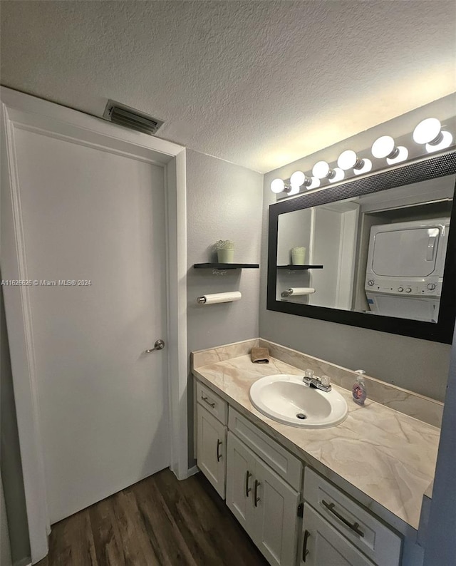 bathroom featuring a textured ceiling, stacked washer and clothes dryer, vanity, and wood-type flooring