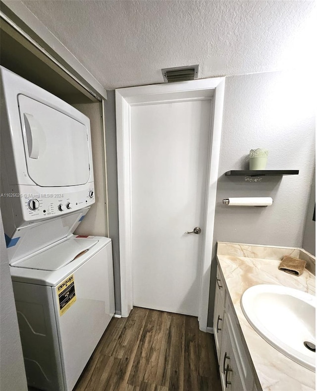 laundry area featuring dark wood-type flooring, stacked washer and dryer, sink, and a textured ceiling