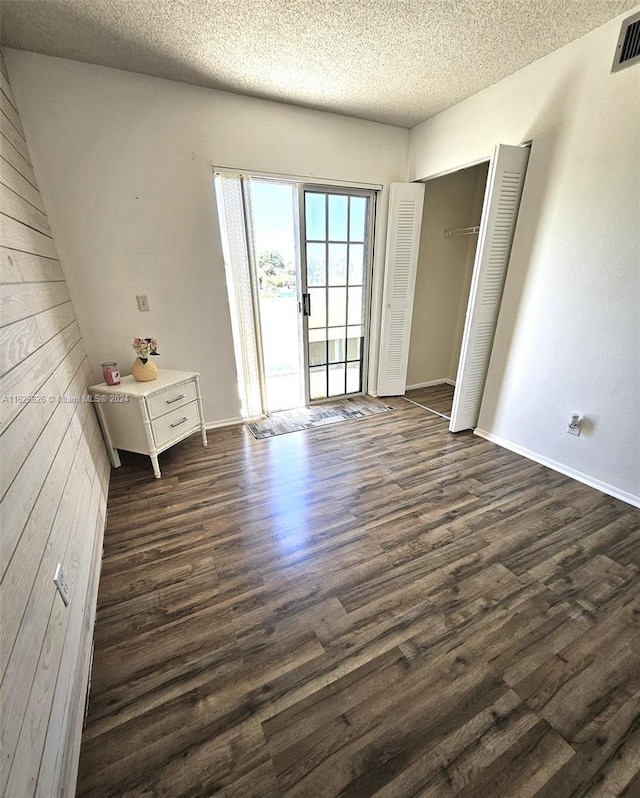 unfurnished bedroom featuring dark wood-type flooring, a closet, a textured ceiling, and access to outside