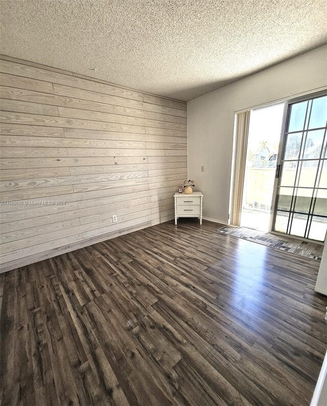 unfurnished room with wooden walls, a textured ceiling, and hardwood / wood-style flooring