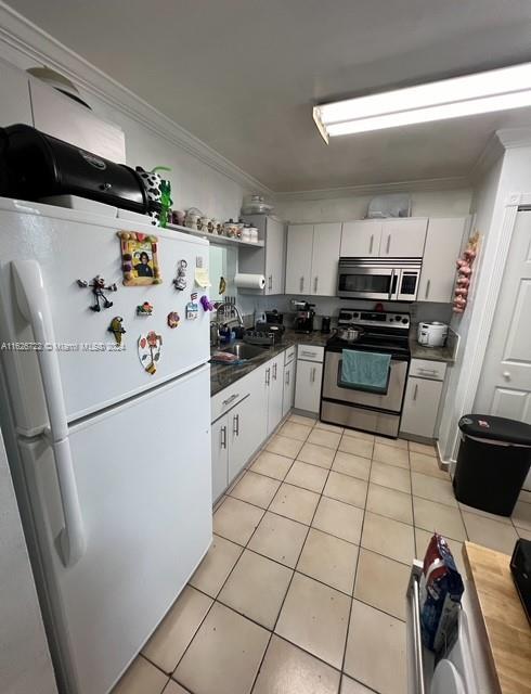 kitchen with white cabinetry, ornamental molding, stainless steel appliances, and light tile patterned flooring