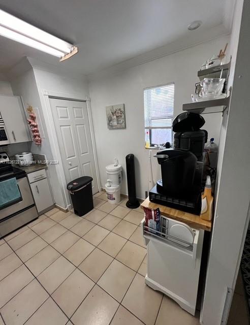 kitchen with white cabinets, stainless steel range with electric stovetop, ornamental molding, and light tile patterned floors