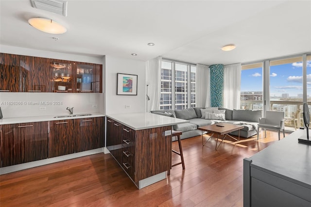 kitchen with sink, dark wood-type flooring, a breakfast bar, expansive windows, and kitchen peninsula