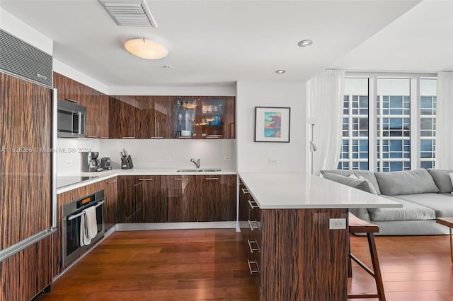 kitchen with sink, appliances with stainless steel finishes, dark hardwood / wood-style floors, a center island, and a kitchen bar