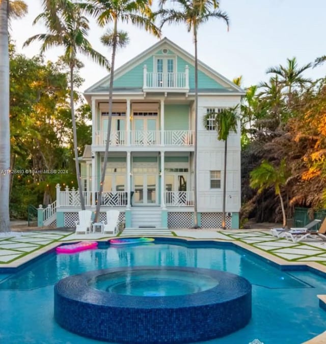 back of property featuring a balcony and a swimming pool with hot tub