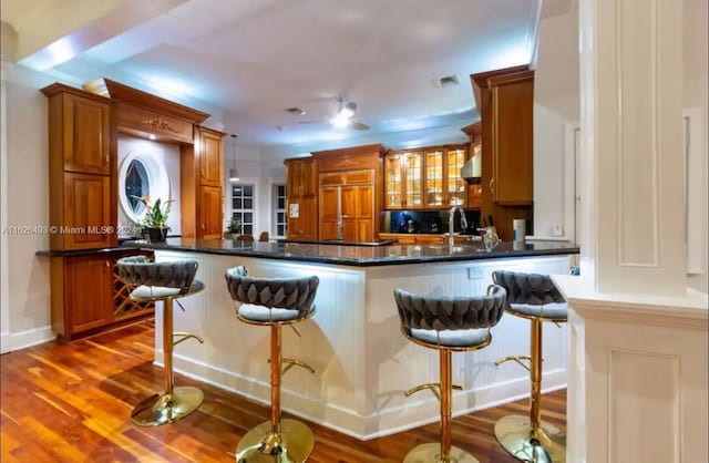 kitchen with sink, a breakfast bar area, wood-type flooring, paneled built in fridge, and kitchen peninsula