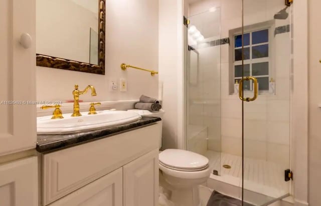 bathroom featuring toilet, vanity, and a shower with shower door