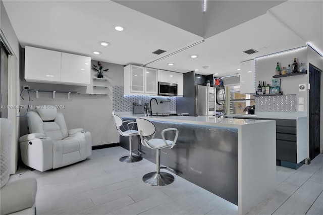 kitchen with white cabinets, a kitchen bar, appliances with stainless steel finishes, light hardwood / wood-style flooring, and backsplash