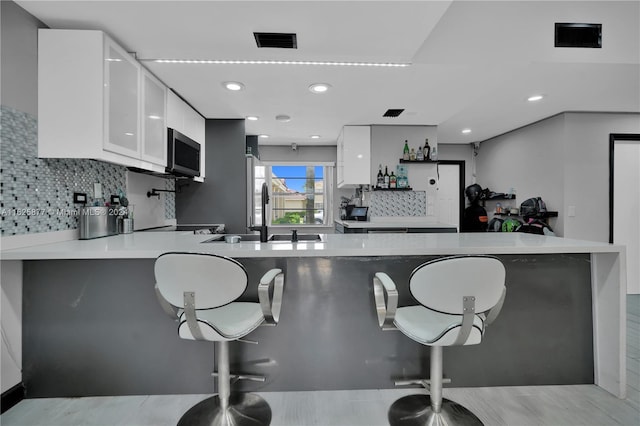 kitchen with kitchen peninsula, white cabinets, backsplash, appliances with stainless steel finishes, and sink